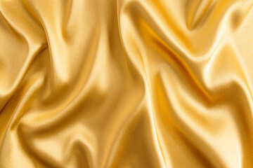 Fototapeta premium Elegant satin fabric with a golden color. The luxurious texture of the soft folds of the fabric. The concept of a festive background. design.