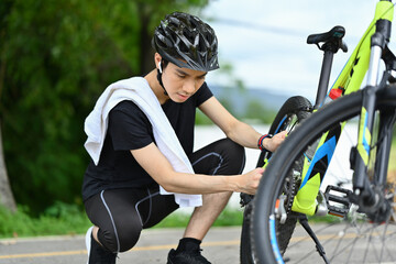Naklejka premium Concentrated young cyclist repairing his bike in the public park