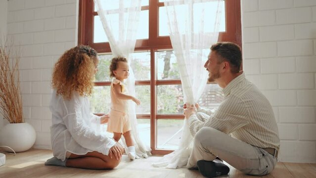 Cheerful parents playing with daughter together in living room at home. Father and mother take care give time to little baby in bedroom at house. Family relationship concept.