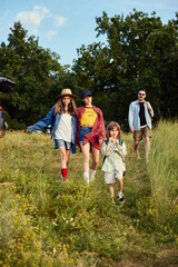 Young people, man and woman going hiking, walking with children on warm summer day. Beautiful nature scenery, fresh air. Concept of leisure time, fun, nature, active lifestyle, family, travel