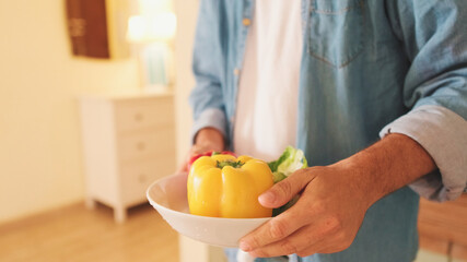 Close-up of the hands of guy dressed in denim shirt cooking sandwich while standing in the kitchen