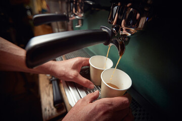 top view of caucasian male hands holding two paper cups below the jet of black coffee