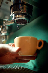 caucasian male hand holding cup below the of espresso coffee machine