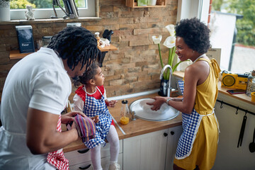 Fototapeta na wymiar Family Harmony in the Kitchen: Mother Washing Dishes, Father Drying, and a Little Girl Indulging in a Sweet Tre