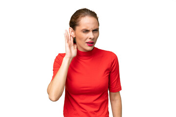 Young caucasian woman over isolated background listening to something by putting hand on the ear