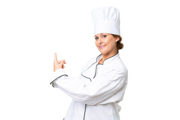 Middle-aged chef woman over isolated background pointing back