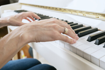 Close-up of female hands on piano keys. A woman with French manicure plays the piano. Musician with musical instrument learning music.