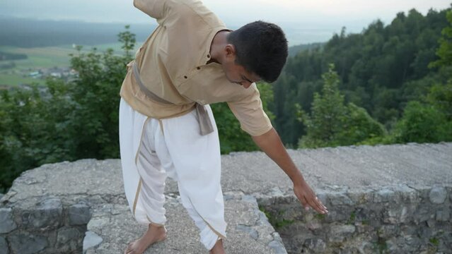 Eyes-closed Indian man doing meditation in the morning at hill top with sunrise in the background on stone wall of castle ruins