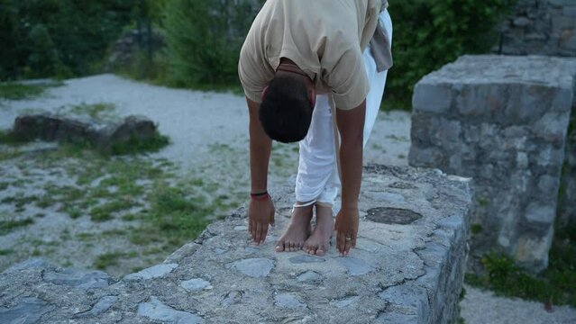 Indian man stretching before doing the hatha yoga meditation standing before castle ruins at sunrise