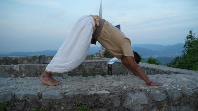 Asian men doing a hatha yoga pose at dawn on top of the stone wall
