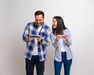 Young girlfriend playing video game and looking cheerfully at boyfriend's mobile phone. Excited couple enjoying gaming and competing each other while standing against background