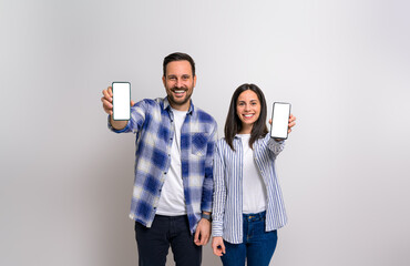 Young couple smiling and showing blank screens of smart phones for advertisements. Cheerful man and woman promoting cellphones with empty free space against background