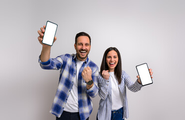 Portrait of excited girlfriend with boyfriend laughing and pumping fists while showing mobile...