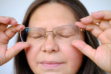 close-up female face of elderly woman 50 years old with long hair in glasses, tired eyes closed,...