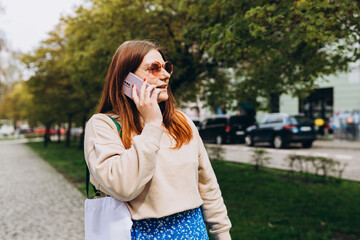 Outdoor lifestyle fashion portrait of woman talking on phone on the street. Close up of woman using smartphone outdoors. Urban lifestyle concept