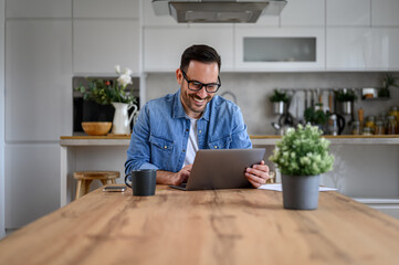 Cheerful young handsome man with glasses on working over laptop on desk, sitting at the home office