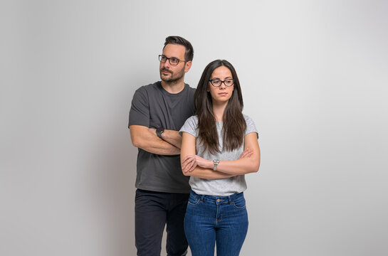 Thoughtful young couple with arms crossed standing confidently against isolated background. Contemplative man and woman wearing eyeglasses and casuals looking away seriously - Powered by Adobe