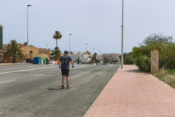 a man rollerblading down the road with his back to the camera - obrazy, fototapety, plakaty
