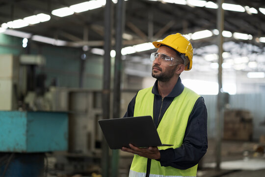 Male engineer worker working with clipboard and control machine in factory. Male worker working with CNC machine with safety uniform, helmet in industry factory