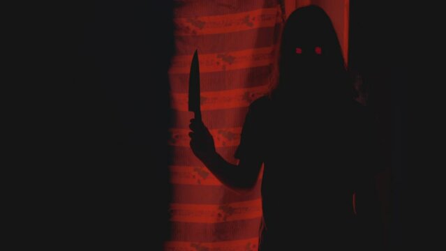 Hiding from the killer ghost with glowing eyes and a knife. Vintage horror. Red light. Backlit silhouette. Halloween video. Handheld camera. Video transition.