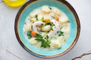 Turquoise bowl with creamy chicken and potato gnocchi soup, top view on a white granite background, horizontal shot