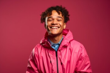 Medium shot portrait photography of a grinning boy in his 30s wearing a lightweight windbreaker against a hot pink background. With generative AI technology