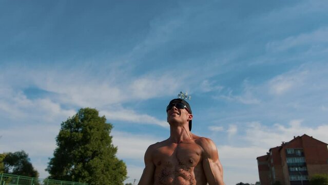 Young muscular man with naked torso demonstrates large biceps and abdos after exercising in stadium. Slow motion