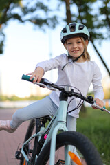 Cheerful girl rides a bicycle in a helmet along the bike path in the park.