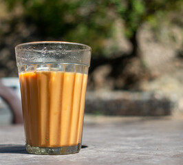 A close up shot of a milk tea in a traditional transparent glass. Road side place or Tapri in India.