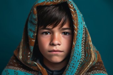 Close-up portrait photography of a tender boy in his 30s wearing a unique poncho against a teal blue background. With generative AI technology