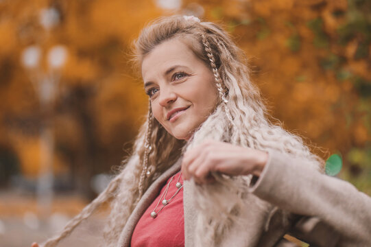 Attractive middle age woman in trendy coat in front of autumn leaves enjoys warm weather. Mature woman walks in the autumn park and enjoys an active life.