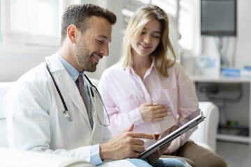 Male doctor showing tablet with healthcare results to young pregnant woman, gynecology service and...