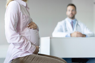 Obraz premium Closeup of woman expecting baby having appointment with doctor in clinic prenatal healthcare center, focus on lady holding hands on baby bump in doc office