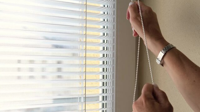 opening window blinds. lowering window shades. Sunlight behind horizontal blinds. Hand opening venetian blinds slats with finger on house. Woman looking through blinds