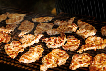 Pork steaks cooking in open flame on barbecue grill.