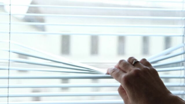 opening window blinds. lowering window shades. Sunlight behind horizontal blinds. Hand opening venetian blinds slats with finger on house. Woman looking through blinds