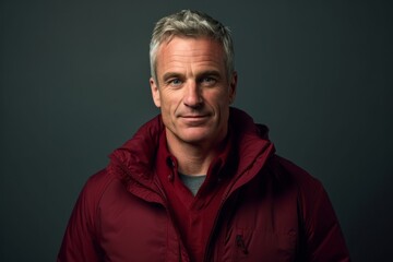 Fototapeta premium Headshot portrait photography of a beautiful mature man wearing a lightweight windbreaker against a rich maroon background. With generative AI technology