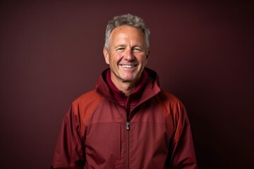 Obraz premium Lifestyle portrait photography of a grinning mature man wearing a lightweight windbreaker against a rich maroon background. With generative AI technology