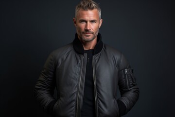 Lifestyle portrait photography of a tender mature man wearing a sleek bomber jacket against a dark grey background. With generative AI technology