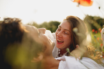 Obraz premium The close portrait of wedding couple laying at the poppies field laughing smiling