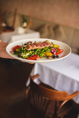 Nicoise salad with tuna, asparagus, tomatoes and a glass of white wine on a large white plate.
