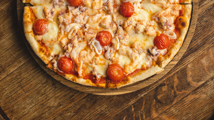 Appetizing Italian pizza with seafood, tomatoes and cheese on a wooden board.