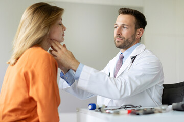 Professional male doctor examining thyroid gland of female patient during checkup in private...