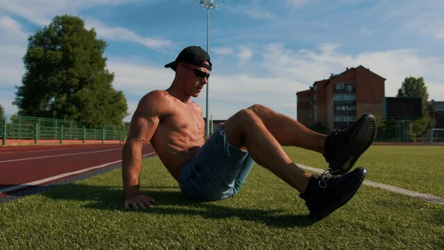 Young muscular man training at the city stadium and does exercises on the press by rearranging his legs