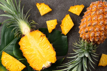 Fresh cut pineapple with tropical leaves on dark gray table background.