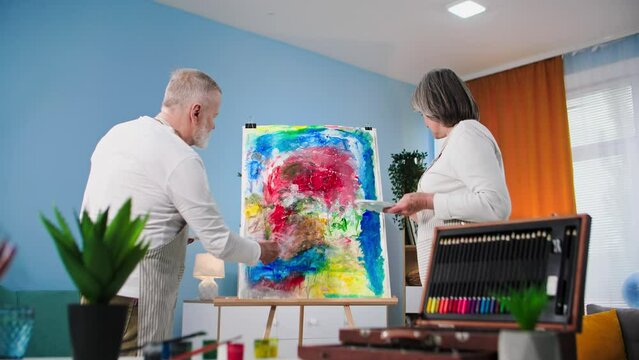 modern pensioners, talented old man together with his wife paint a creative picture with brushes and paints at home