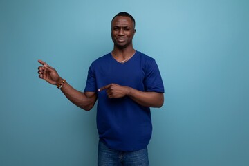 handsome friendly young african man in a blue t-shirt shows his hand towards the empty space