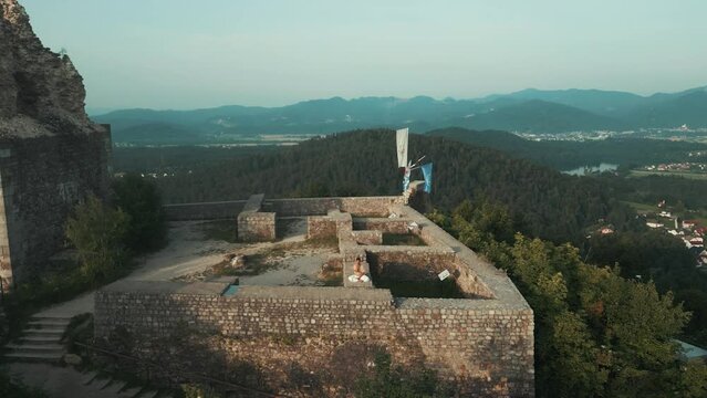 Drone shot of Indian man sitting in hatha yoga pose and meditating nadhi shuddhi on stone castle wall on top of the hill surrounded by hills fields lake and forests in the morning at sunrise