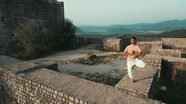 orbit slow motion shot of Asian Indian male doing yoga pose reveling the castle behind him at sunrise