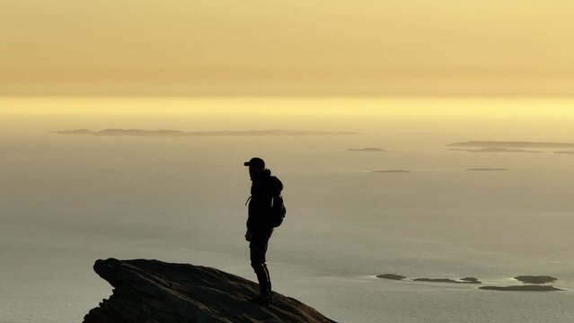 Climber silhouette on arctic mountain lift arms n midnight sun; drone zoom